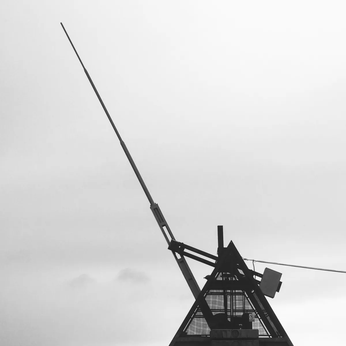 Photo noir et blanc du métronome de Prague, une structure métallique aux allures d'un métronome comportant une énorme aiguille mécanisée battant un lent tempo.